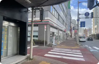 バス停を降りたら、本町通り商店街（ぷらっと本町）のアーケード方向へまっすぐ進み、セブンイレブンが見えたら左折してください。